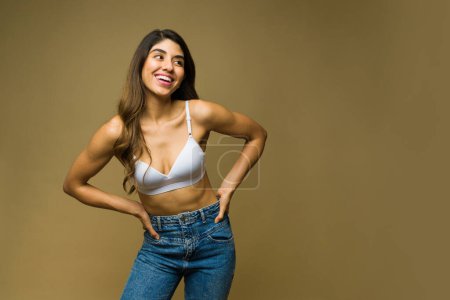 Foto de Mujer joven fitness con un cuerpo atlético que se pone la ropa y se prepara con un sujetador y jeans - Imagen libre de derechos