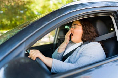 Téléchargez les photos : Somnolent gros latino femme bâillant et à la recherche fatigué après la conduite et les déplacements dans sa voiture - en image libre de droit