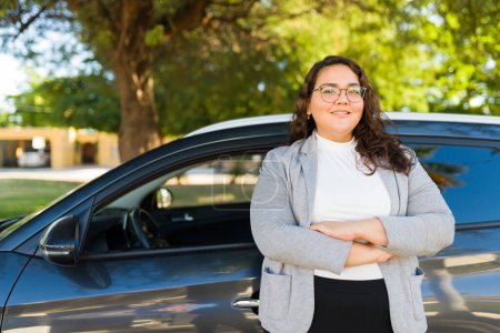 Schöne hispanische dicke Fahrerin sieht glücklich aus, während sie sich auf ihr Auto stützt, während sie vor der Fahrt im Freien steht 