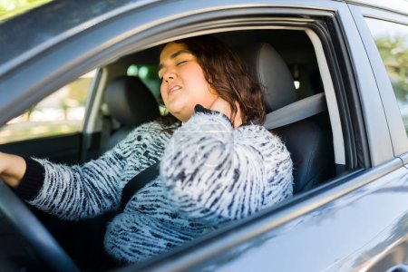 Photo for Tired stressed fat woman rubbing her back and suffering from neck pain while driving her car and commuting to work - Royalty Free Image