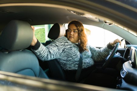 Foto de Conductora con sobrepeso cuidadoso girando hacia atrás y mirando detrás de su coche mientras conduce y viaja - Imagen libre de derechos