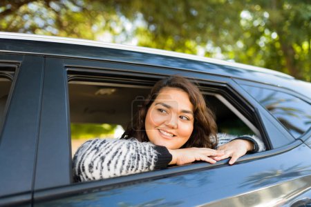 Photo for Relaxed young woman and passenger looking out the car window while taking a ride and traveling looking happy - Royalty Free Image
