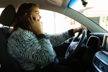 Photo for Hispanic big woman behind the wheel driving and smiling while talking on the smart phone - Royalty Free Image
