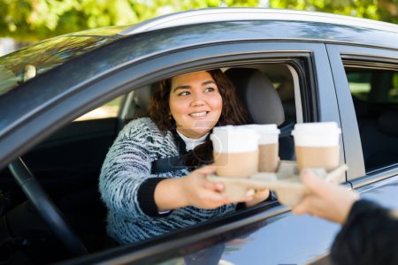 Téléchargez les photos : Belle femme latine obèse conduisant sa voiture sur un à travers un lecteur à travers l'achat de café pour aller - en image libre de droit