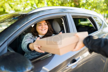 Téléchargez les photos : Heureuse grosse femme souriante tout en recevant un paquet tout en conduisant sa voiture - en image libre de droit