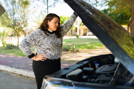 Téléchargez les photos : Stressé grosse femme ouvrant le capot et vérifiant le moteur de sa voiture cassée après avoir conduit - en image libre de droit