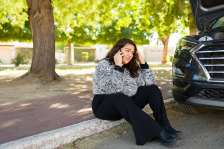 Foto de Mujer obesa estresada sentada en el lado del paseo pidiendo ayuda debido a su coche dañado - Imagen libre de derechos