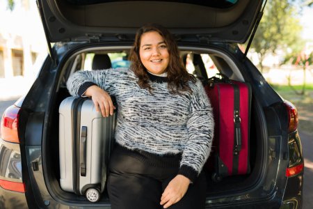 Téléchargez les photos : Belle femme obèse prête à voyager en voiture et à mettre ses valises sur le coffre - en image libre de droit