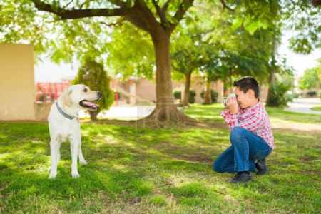 Téléchargez les photos : Jeune garçon prenant des photos et des photos au parc de son adorable chien jaune retriever tout en jouant à un jeu - en image libre de droit