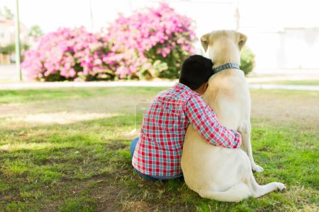 Adorable kid hugging a beautiful yellow labrador dog and giving love to his friend while relaxing together in the park