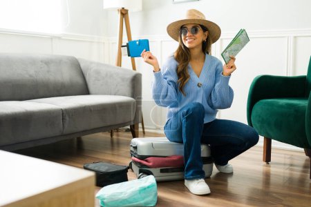 Téléchargez les photos : Belle jeune femme avec un chapeau d'été souriant et prêt pour ses vacances seul tout en préparant sa valise - en image libre de droit