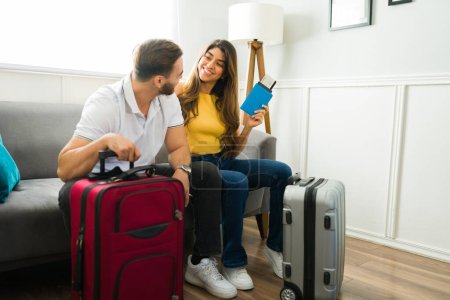 Foto de Hermosa mujer hispana sonriendo a su novio mientras espera en casa con sus maletas para irse de vacaciones - Imagen libre de derechos