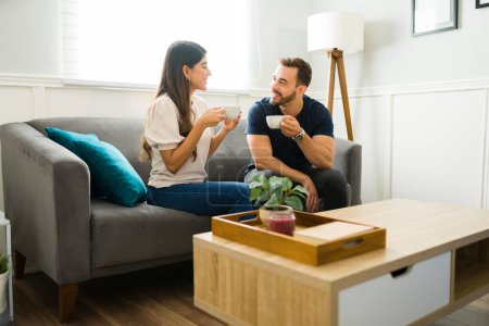 Téléchargez les photos : Souriant jeune femme et homme bavardant tout en buvant du café lors d'un rendez-vous à la maison - en image libre de droit