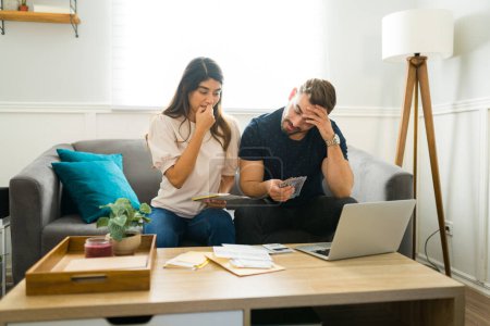 Photo for Worried couple looking anxious and paying their debts and stressed about their finances at home - Royalty Free Image