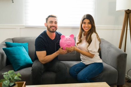Photo for Cheerful smiling couple holding a piggy bank while saving money together and making eye contact - Royalty Free Image