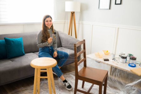 Foto de Mujer atractiva feliz haciendo un proyecto de bricolaje en casa y listo para pintar un taburete y una silla - Imagen libre de derechos