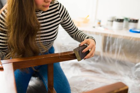 Téléchargez les photos : Gros plan d'une jeune femme latine faisant des meubles retournant et réparant une chaise avec du papier de verre pour la peindre - en image libre de droit