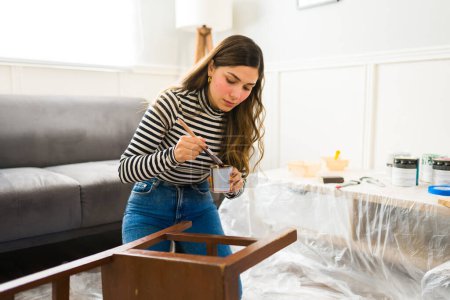 Foto de Mujer atractiva haciendo mejoras y renovaciones en el hogar mientras pinta una silla en casa - Imagen libre de derechos