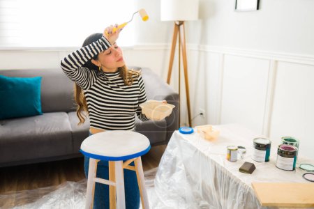 Téléchargez les photos : Femme fatiguée regardant épuisé tout en peignant un tabouret de chaise tout en travaillant sur ses meubles flipping entreprise - en image libre de droit