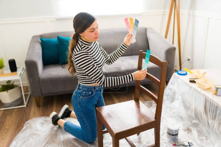 Téléchargez les photos : Femme hispanique choisissant une couleur pour peindre une chaise tout en réparant des meubles à la maison - en image libre de droit