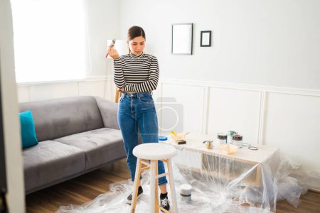 Téléchargez les photos : Belle jeune femme peignant une chaise de tabouret tout en faisant la restauration de meubles bricolage à la maison - en image libre de droit