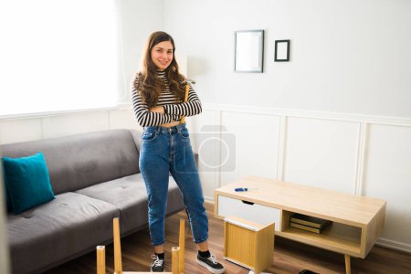 Téléchargez les photos : Toute la longueur d'une femme heureuse se sentant fière d'assembler des meubles avec des outils à la maison - en image libre de droit