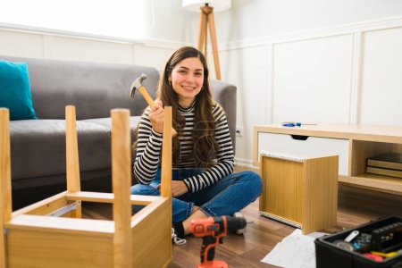 Téléchargez les photos : Femme joyeuse souriant tenant un marteau tout en faisant et assemblant de nouveaux meubles - en image libre de droit