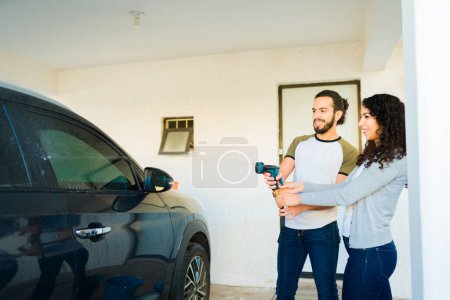Téléchargez les photos : Couple joyeux en utilisant un tuyau de pulvérisation d'eau ensemble tout en lavant la voiture au garage à la maison - en image libre de droit