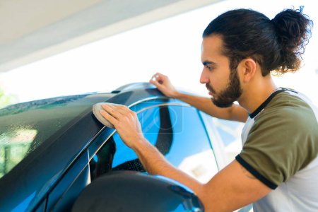 Téléchargez les photos : Jeune homme mexicain polissant et détaillant sa voiture après l'avoir lavée à l'extérieur - en image libre de droit