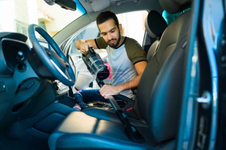 Photo for Latin young man washing the car and using a vacuum cleaner to clean her sets and car interior - Royalty Free Image