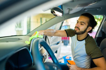 Photo for Handsome hispanic man cleaning the car interior while washing the car in the home garage - Royalty Free Image