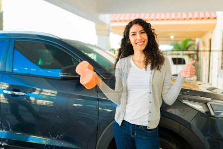 Foto de Mujer joven emocionada terminando de lavar el coche y haciendo un pulgar hacia arriba buscando feliz - Imagen libre de derechos