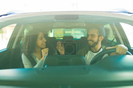 Téléchargez les photos : Heureux couple souriant avoir du plaisir à jouer à un jeu tout en conduisant dans la voiture de prendre une route - en image libre de droit