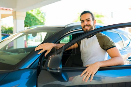 Téléchargez les photos : Attrayant homme hispanique ouvrir la porte et monter dans la voiture dans son garage à la maison - en image libre de droit