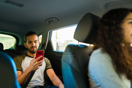 Téléchargez les photos : Jeune homme attrayant passager faisant un voyage avec un conducteur d'un service d'application de covoiturage et textos - en image libre de droit
