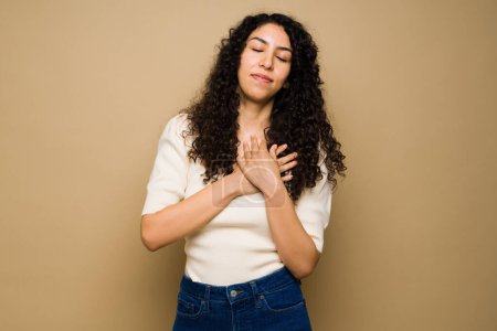 Foto de Attractive latin woman with her hands on her heart and chest feeling love and thankful while having positive emotions - Imagen libre de derechos