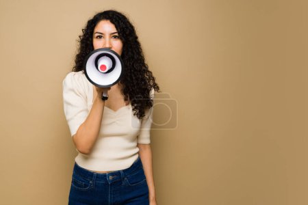 Foto de Portrait of a latin young woman making eye contact and using a megaphone to give a message or announcement ad - Imagen libre de derechos