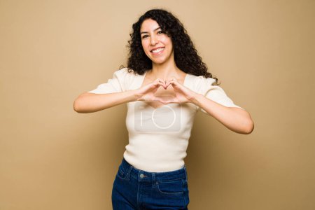 Foto de Loving latin young woman smiling making a heart with her hands in the chest and feeling in love - Imagen libre de derechos