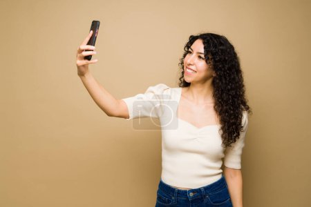 Foto de Beautiful young woman smiling and taking a selfie with her smartphone to post it on social media - Imagen libre de derechos