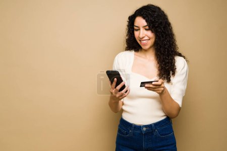 Téléchargez les photos : Beautiful happy woman smiling while doing online shopping on her smartphone and paying with a credit card - en image libre de droit