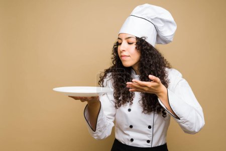 Téléchargez les photos : Young woman chef or cook with curly hair smelling the delicious food against a studio background - en image libre de droit