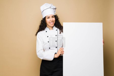 Téléchargez les photos : Happy woman chef or cook holding a blank banner showing the food menu or ad about a restaurant - en image libre de droit