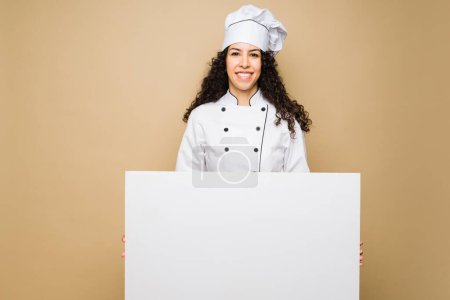 Foto de Cheerful beautiful woman chef holding a blank banner to show the restaurant food menu - Imagen libre de derechos