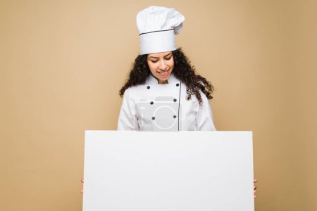 Téléchargez les photos : Mexican young chef with curly hair smiling holding a blank banner with the restaurant food menu - en image libre de droit