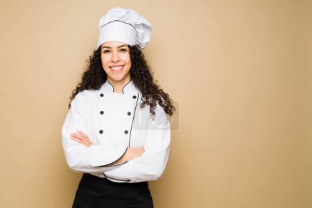 Photo for Beautiful latin young woman working as a chef or cook looking happy in front of a studio background with copy space - Royalty Free Image