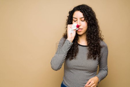Photo for Sick hispanic woman in her 20s suffering from a nose bleed and looking sick - Royalty Free Image