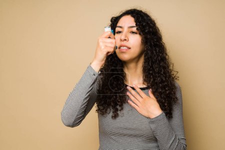 Téléchargez les photos : Mexican young woman with curly hair having an asthma attack and breathing problems while using an inhaler - en image libre de droit