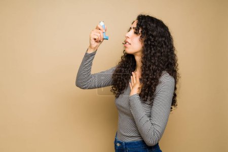 Sick hispanic woman having an asthma attack and breathing problems while using an inhaler
