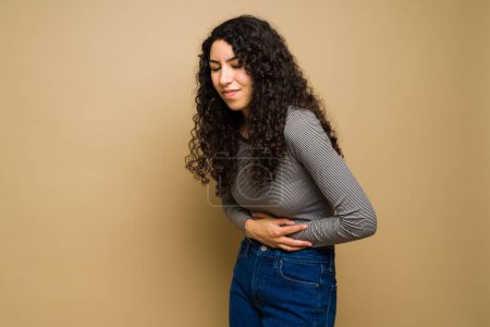 Photo for Upset sick young woman holding her stomach abdomen while suffering from cramps during her period - Royalty Free Image