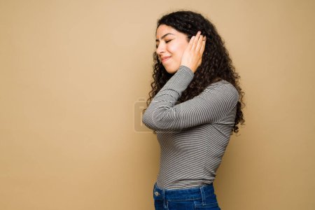Photo for Latin sick young woman suffering from pain in her ears because of an infection in front of a studio background - Royalty Free Image